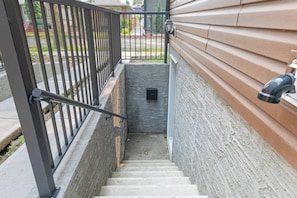 A residential staircase with a metal railing, a stone wall, and a light fixture on the right.