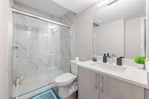 Ein modernes Badezimmer mit einer gläsernen Duschkabine, einer weißen Toilette, einem Waschbecken mit Spiegel und einer kleinen Topfpflanze.