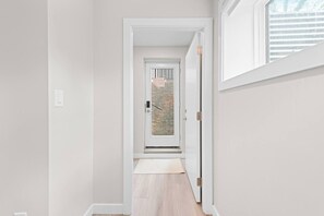 A narrow hallway with a door leading to a room with a window.