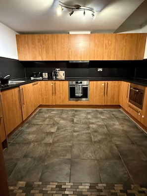 A kitchen with wooden cabinets, a black countertop, a stainless steel oven, and a tiled floor. - Luxurious Mailbox Penthouse 3 Bedrooms 3 Bathrooms (Birmingham)