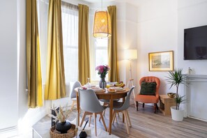 A dining area with a round table, chairs, a vase with flowers, and a fruit bowl. - Spacious 2BR South  London Retreat  Great Transport (London)