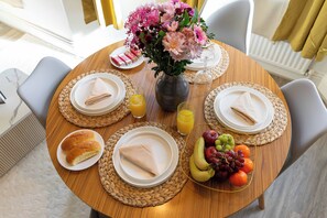 Ein runder Esstisch mit Tellern, Servietten, einer Blumenvase, einem Glas Orangensaft und einer Obstschale.