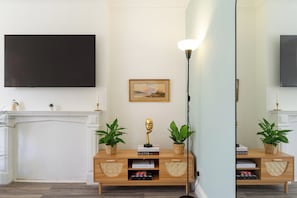 A living room with a flat-screen TV mounted on the wall, a fireplace, a floor lamp, and a wooden console table with decorative items and plants. - Spacious 2BR South  London Retreat  Great Transport (London)
