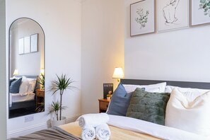 Ein Hotelzimmer mit Bett, Nachttisch, Lampe, Spiegel und Wandbildern.