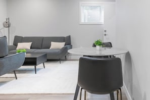 A modern living room with a grey sofa, a round dining table, and a black chair.