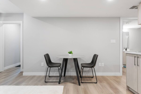 A modern kitchen with a white countertop, two black chairs, and a small potted plant on the table.