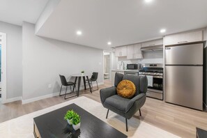 A modern kitchen with stainless steel appliances, a dining area with a round table and chairs, and a grey armchair with a decorative pillow. - Stylish 1BR Guest Suite | Near UofA, Whyte & DT - Double Room (Edmonton)