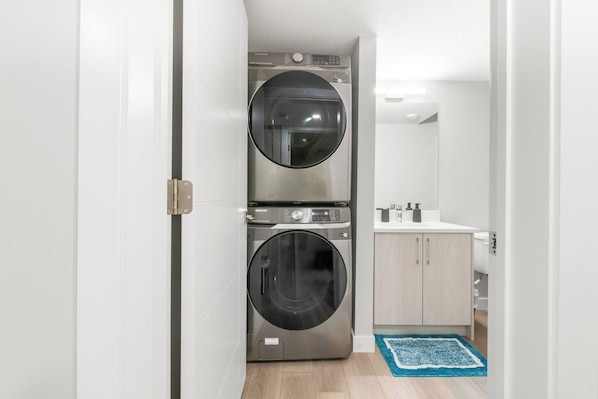 Una sala de bugaderia amb dues piles de rentadores i assecadores frontals, un bany amb productes de higiene personal, i una catifa blava al terra.