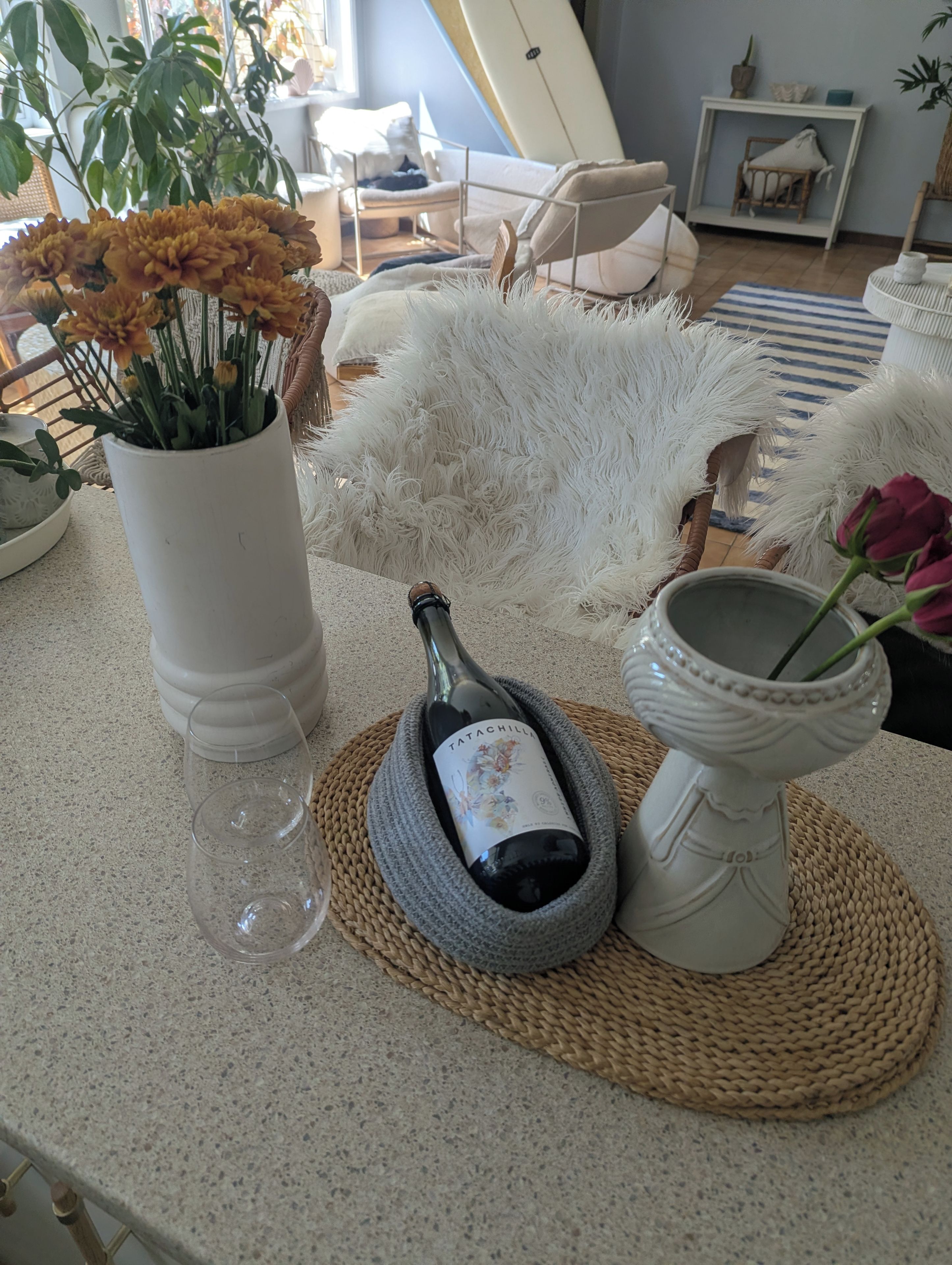 A room with a surfboard leaning against the wall, a white furry chair, and a woven placemat on the floor.