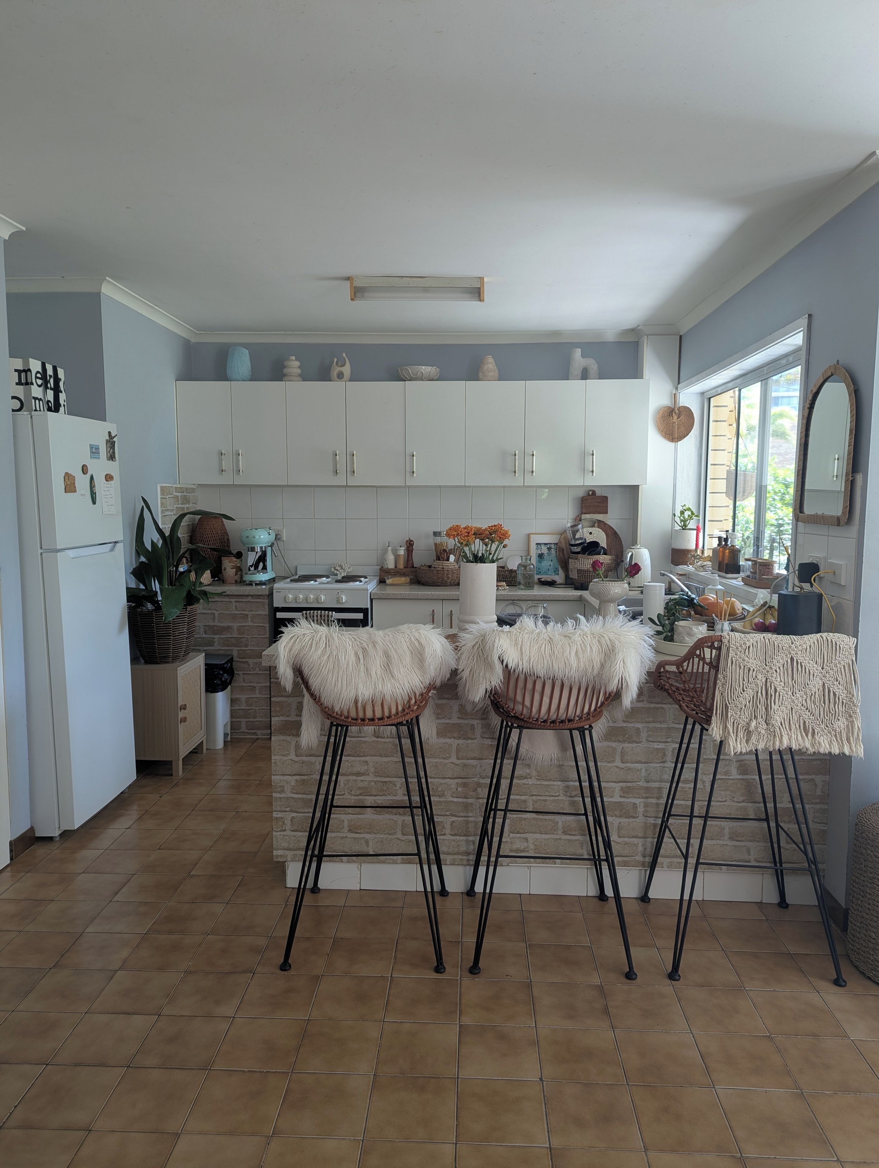 A kitchen with white cabinets, a central island with stools, and a window with a view.