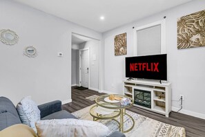 Ein modernes Wohnzimmer mit einem Flachbildfernseher, der 'NETFLIX' anzeigt, einem Sofa, einem Couchtisch und einem Kamin.