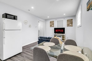 Ein modernes Wohnzimmer mit einem Glastisch, grauen Sofas, einem Flachbildfernseher und einem weißen Kühlschrank.