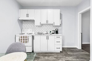 A compact kitchen with white cabinets, a stove, and a coffee maker. - Chic Getaway | 1BR Suite w/ Parking & AC (Windsor)