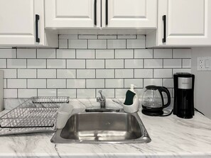 A kitchen with white cabinets, a stainless steel sink, a coffee maker, and a dish soap dispenser. - Chic Getaway | 1BR Suite w/ Parking & AC (Windsor)