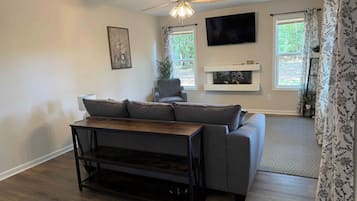 Een woonkamer met een bank, een salontafel, een plafondventilator, een aan de muur bevestigde televisie en een open haard.