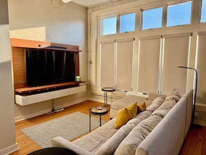 A modern living room with a flat-screen TV, a sofa, a coffee table, and a window with blinds.