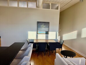 A room with a dining table, chairs, a sofa, and a painting on the wall.