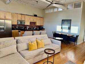 A modern living room with a sofa, a small round table, and a dining area with chairs.