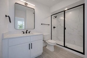 A modern bathroom with a white vanity, a large mirror, a toilet, and a glass-enclosed shower. - Bishop Arts 6BD 6BA Townhouse Parking Sleeps 12 (Dallas)