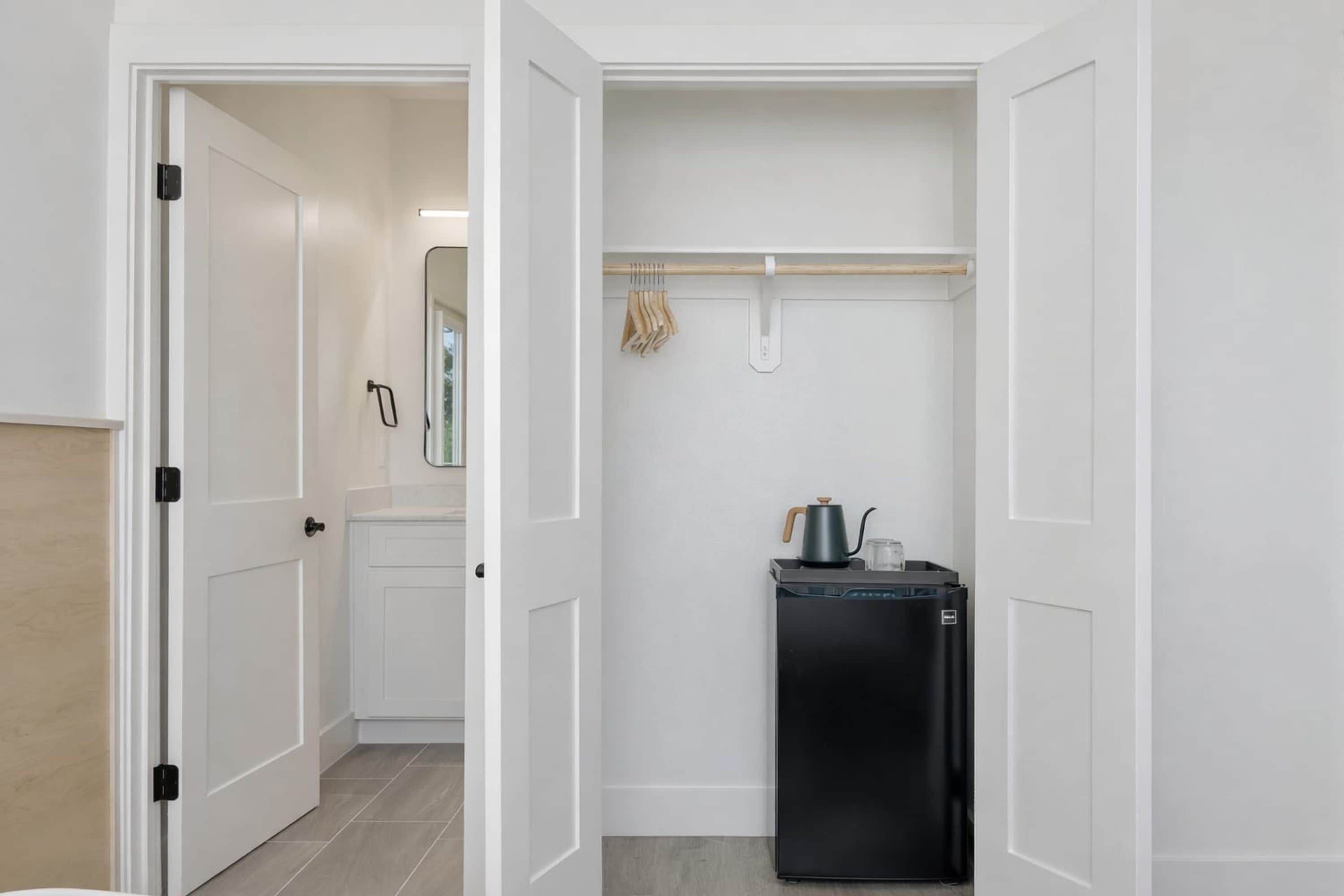 A compact kitchen with a black refrigerator, a kettle, and a hanging clothes rack.