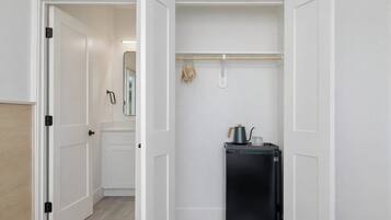 A compact kitchen with a black refrigerator, a kettle, and a hanging clothes rack.