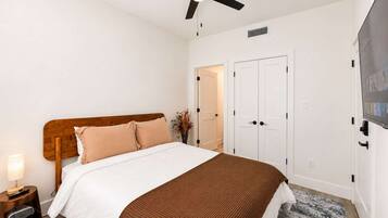 A bedroom with a bed, a ceiling fan, a nightstand with a lamp, a TV, and a door.