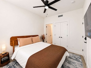 A bedroom with a bed, a ceiling fan, a nightstand with a lamp, a TV, and a door. - Bishop Arts 6BD 6BA Townhouse Parking Sleeps 12 (Dallas)