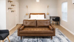 A bedroom with a bed, a brown leather sofa, a small table, a chair, and a ceiling fan. - Bishop Arts Studio w Parking Washer Dryer TV (Dallas)