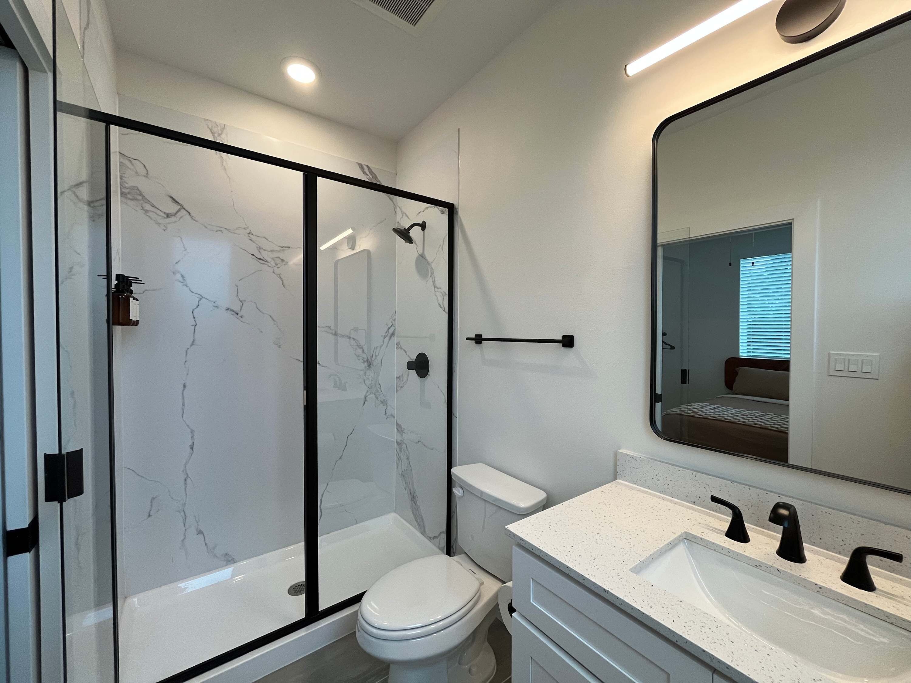 A modern bathroom with a glass-enclosed shower, a white toilet, and a vanity with a large mirror.