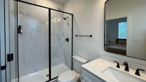 A modern bathroom with a glass-enclosed shower, a white toilet, and a vanity with a large mirror. - Bishop Arts 6BR 6BA Townhouse Sleeps 12 Parking (Dallas)