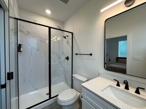 A modern bathroom with a glass-enclosed shower, a white toilet, and a vanity with a large mirror. - Bishop Arts 6BR 6BA Townhouse Sleeps 12 Parking (Dallas)