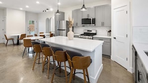 A modern kitchen with a central island, bar stools, stainless steel appliances, and pendant lighting. - Bishop Arts 6BR 6BA Townhouse Sleeps 12 Parking (Dallas)