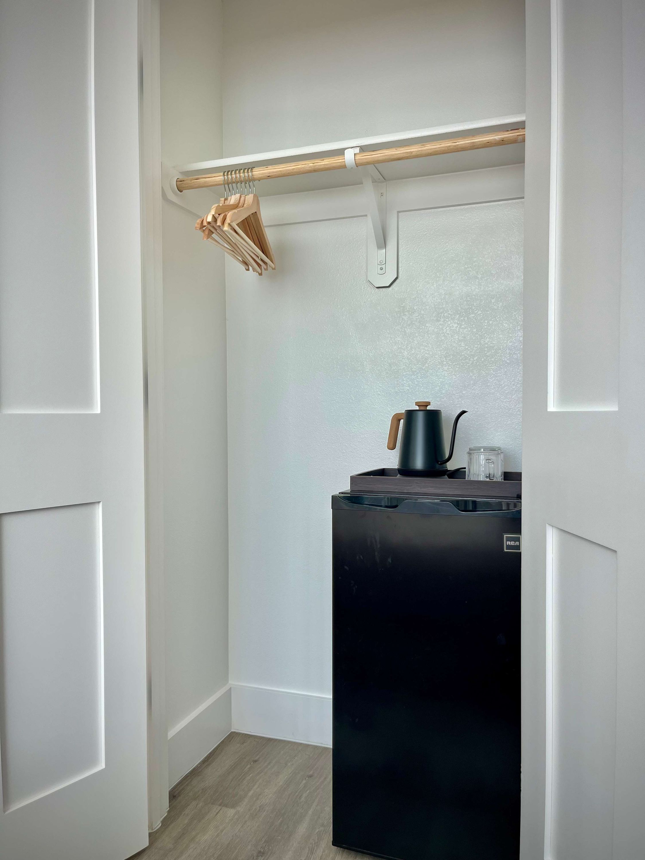 Cocina compacta con un refrigerador negro, un tendedero de madera y una pequeña encimera con un hervidor.