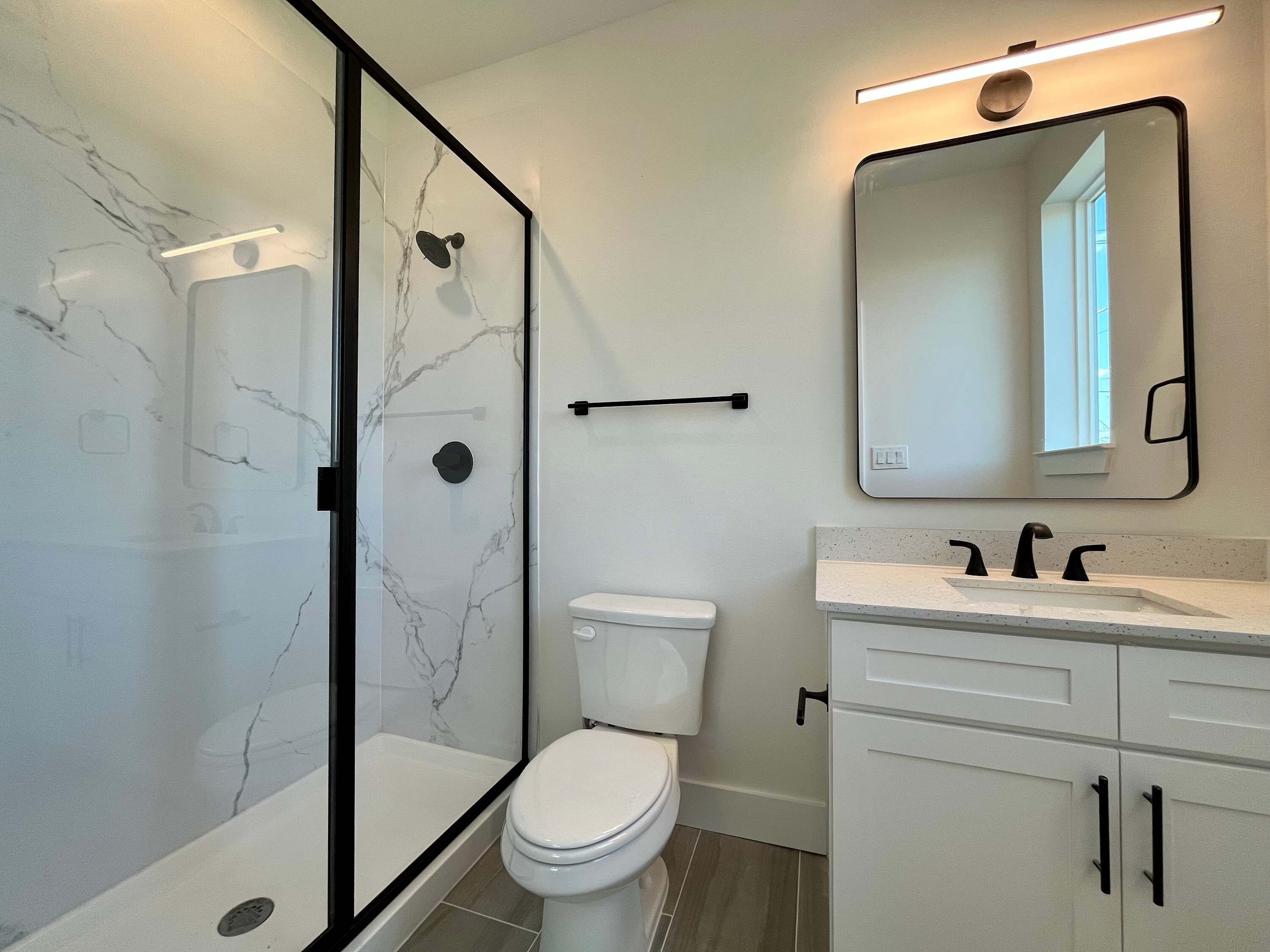 Et stilfuldt badeværelse med bruseniche, toilet, vask med spejl og skab.