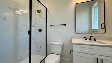 Et stilfuldt badeværelse med bruseniche, toilet, vask med spejl og skab.