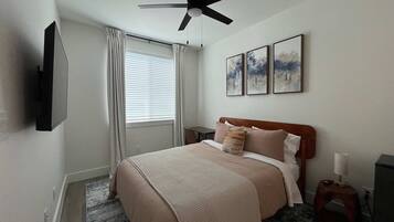 A bedroom with a bed, a ceiling fan, a window with curtains, and three framed pictures on the wall.