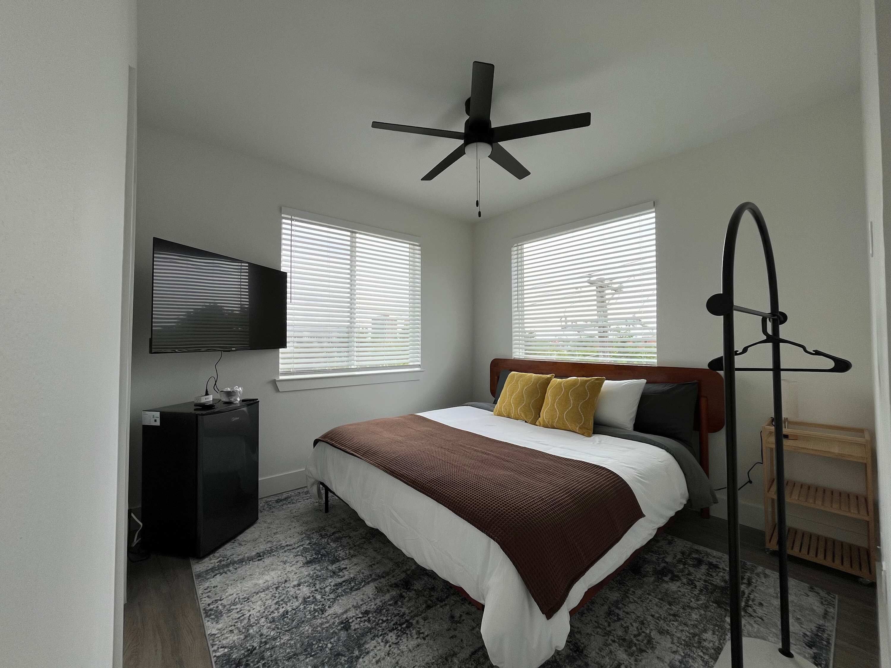 A bedroom with a bed, a ceiling fan, a TV, and a wooden dresser.