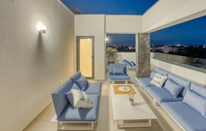 A balcony with blue sofas and a white coffee table, a door leading inside, and a view of the city at night. - Cozy home in Zaton with sauna (Zaton)