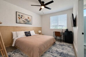 A bedroom with a bed, a ceiling fan, a painting, a desk with a chair, and a television. - Bishop Arts 6BR Townhouse Sleeps 12 Close to DT (Dallas)