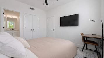 A bedroom with a bed, a desk, a chair, a ceiling fan, a TV, and a window.