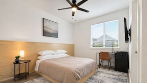 A bedroom with a bed, a desk, a chair, a ceiling fan, a window, and a wall-mounted TV. - Bishop Arts 6BR Townhouse Sleeps 12 Close to DT (Dallas)