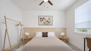 A bedroom with a bed, two bedside tables, a wooden headboard, a wall-mounted artwork, a window with blinds, and a wooden drying rack. - Bishop Arts 6BR Townhouse Sleeps 12 Close to DT (Dallas)