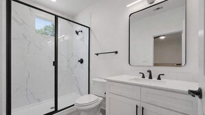 Un baño moderno con ducha envuelta en vidrio, inodoro blanco y tocador con espejo.