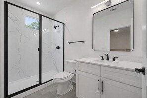 Uma casa de banho moderna com cabine de chuveiro em vidro, sanita branca e toucador com espelho.