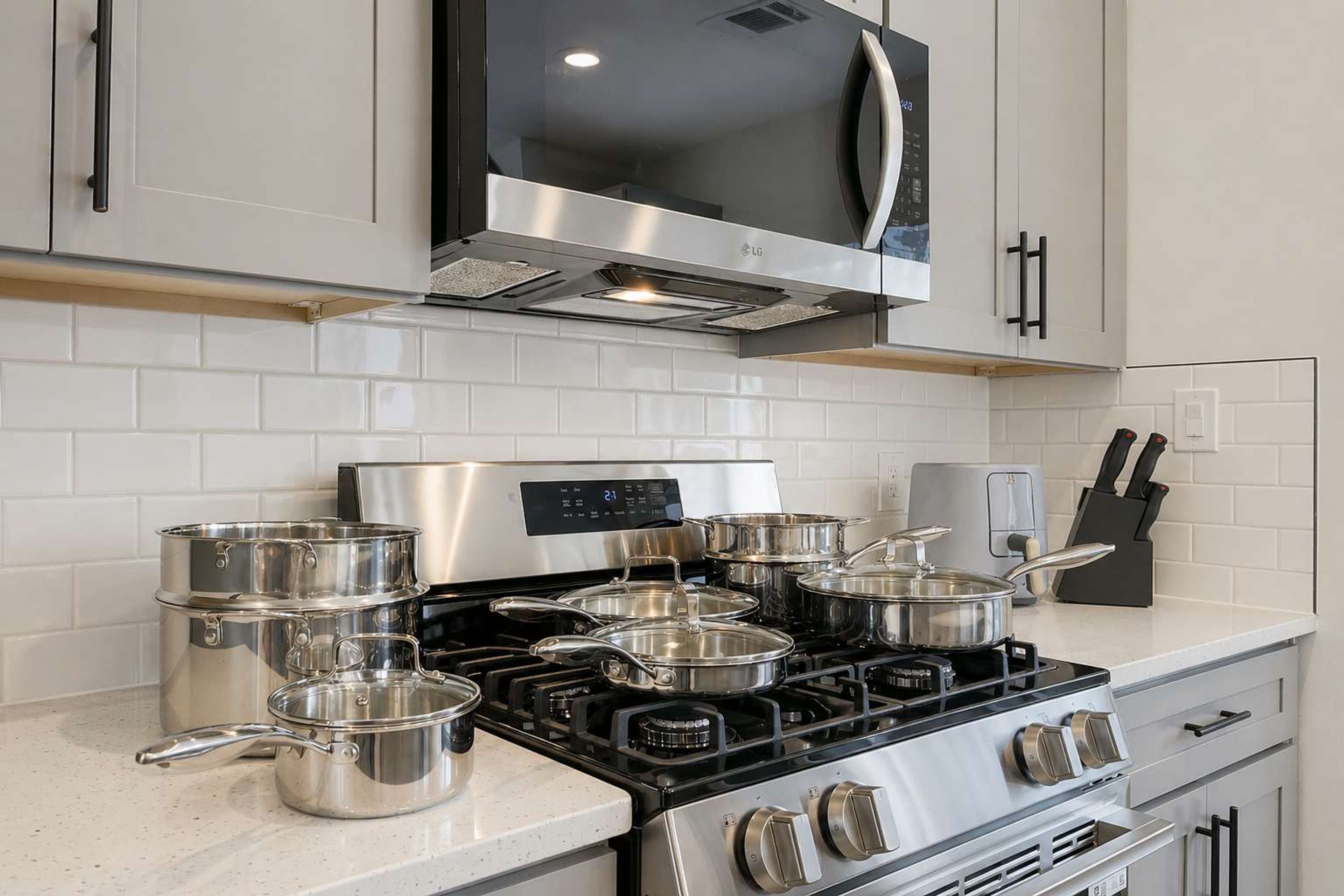 A modern kitchen with stainless steel appliances, including a stove and microwave, and a set of pots and pans.