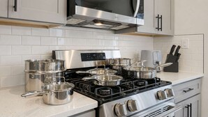 Una cocina moderna con electrodomésticos de acero inoxidable, incluyendo estufa y microondas, y un juego de ollas y sartenes.