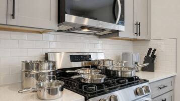 A modern kitchen with stainless steel appliances, including a stove and microwave, and a set of pots and pans.