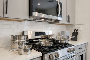 Cozinha moderna com eletrodomésticos de aço inoxidável, incluindo fogão e micro-ondas, e um conjunto de panelas.