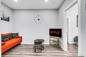 Ein modernes Wohnzimmer mit einer Couch, einem runden Tisch, einem Fernseher auf einem Schrank und einer Wanduhr.