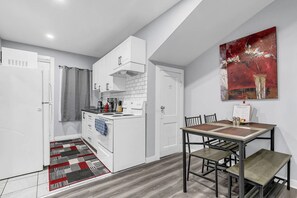 A compact kitchen with white cabinetry, a stove, and a dining area with a table and chairs. - Modern & Private 1-Bedroom Apartment (Windsor)